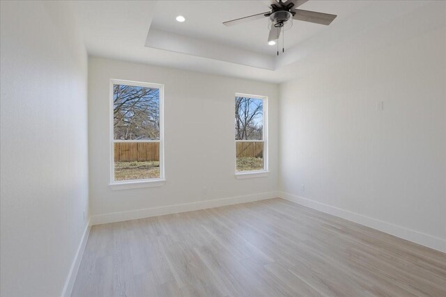 empty room featuring ceiling fan, light hardwood / wood-style flooring, and a raised ceiling