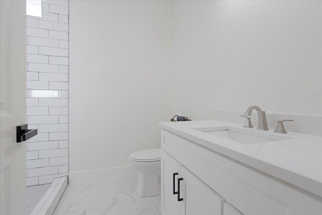 bathroom with toilet, tiled shower, and vanity