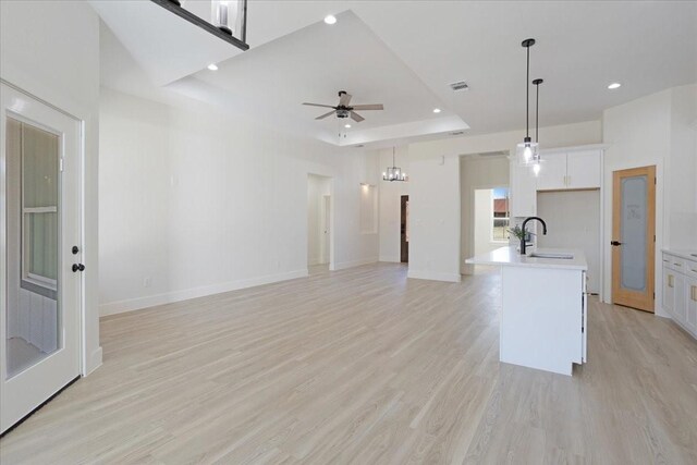 kitchen with white cabinets, decorative light fixtures, sink, a kitchen island with sink, and a tray ceiling