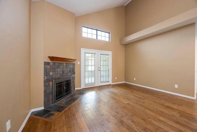 unfurnished living room featuring french doors, hardwood / wood-style flooring, a tile fireplace, and a high ceiling