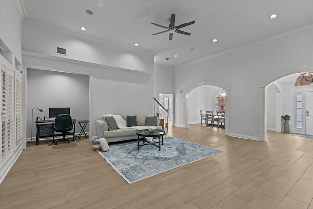 living room with ceiling fan, crown molding, a towering ceiling, and light wood-type flooring