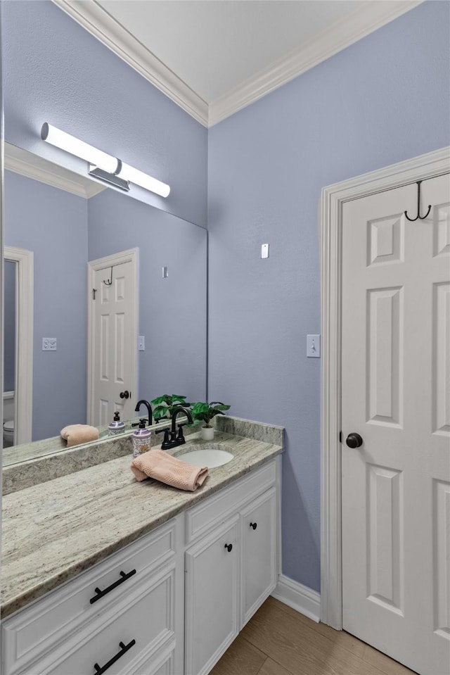 bathroom featuring toilet, ornamental molding, hardwood / wood-style flooring, and vanity