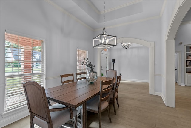 dining room with a raised ceiling, light wood-type flooring, crown molding, and an inviting chandelier