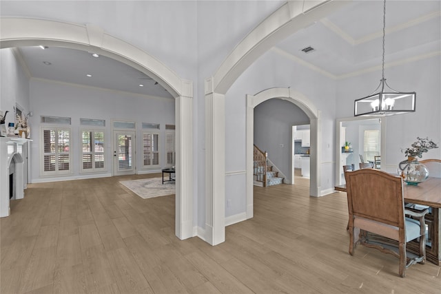 interior space featuring light wood-type flooring, a notable chandelier, a high ceiling, and ornamental molding