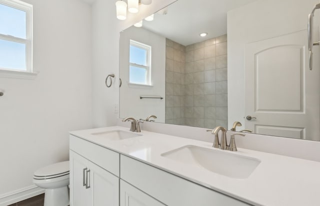 full bath with baseboards, a sink, toilet, and double vanity