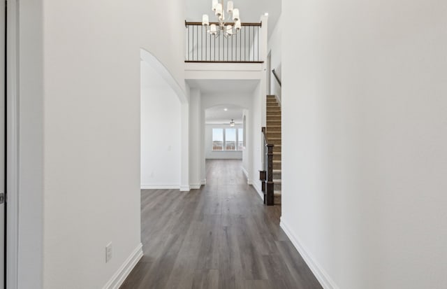 hallway with dark wood-style floors, arched walkways, baseboards, and stairs