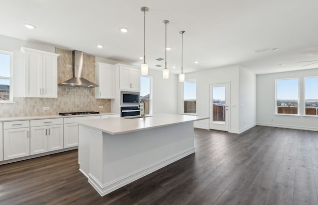 kitchen featuring light countertops, wall chimney range hood, an island with sink, and white cabinetry