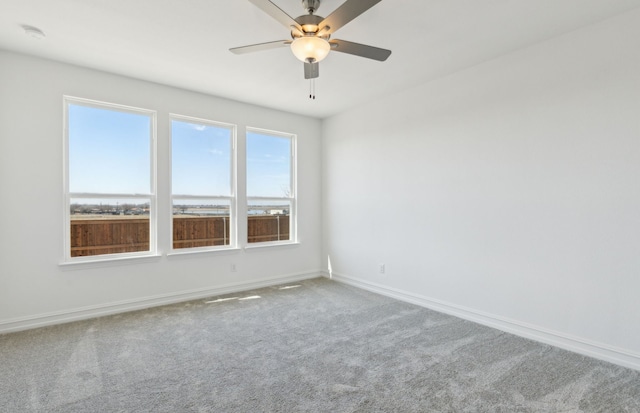 carpeted spare room featuring ceiling fan and baseboards