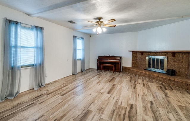 living area featuring visible vents, a fireplace, light wood finished floors, beamed ceiling, and a ceiling fan