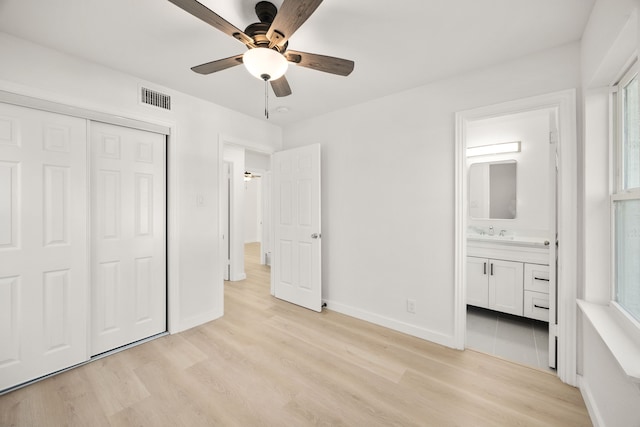 unfurnished bedroom with ensuite bathroom, ceiling fan, a closet, light hardwood / wood-style flooring, and multiple windows