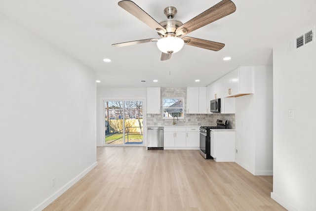 kitchen with ceiling fan, backsplash, white cabinetry, light wood-type flooring, and stainless steel appliances