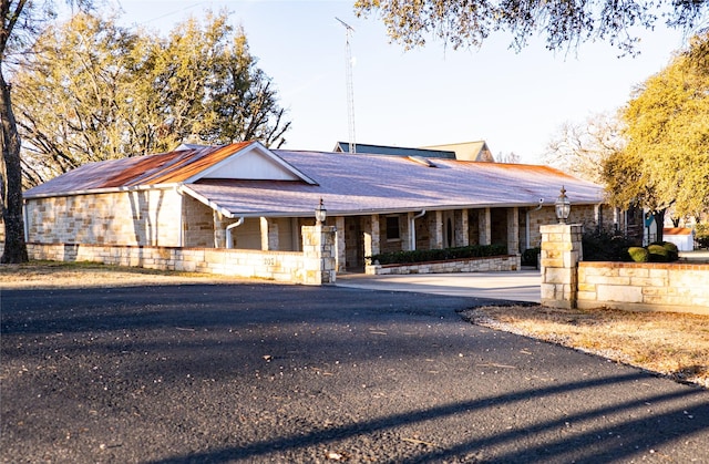 ranch-style house featuring covered porch, a shingled roof, and stone siding
