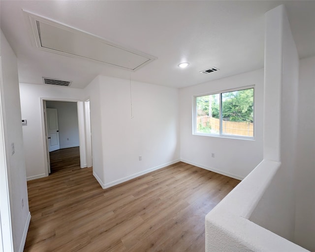 unfurnished room featuring visible vents, wood finished floors, attic access, and baseboards