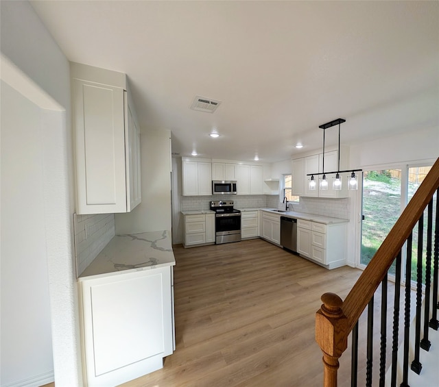 kitchen featuring visible vents, light stone counters, stainless steel appliances, white cabinetry, and pendant lighting