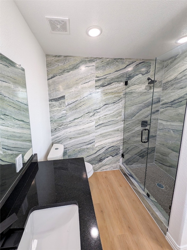 bathroom featuring toilet, a sink, wood finished floors, visible vents, and a stall shower