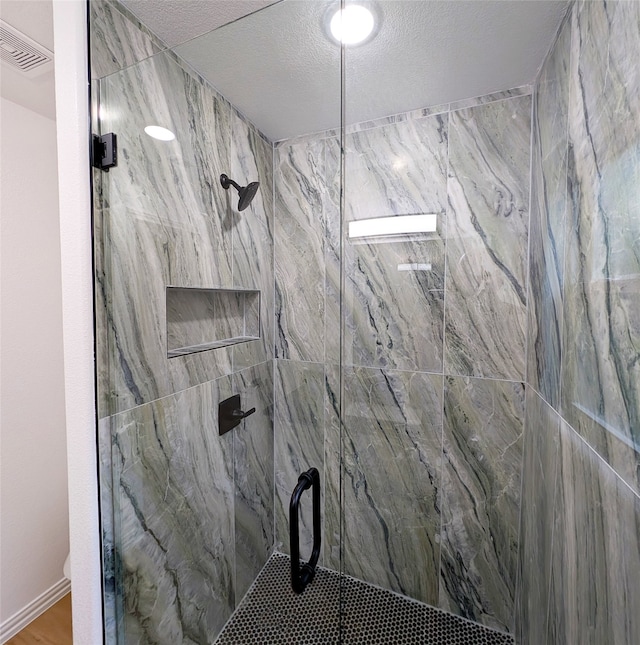 bathroom featuring a textured ceiling, a marble finish shower, and visible vents