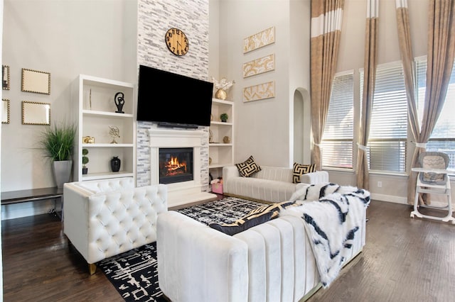 living room with built in features, dark hardwood / wood-style floors, a stone fireplace, and a high ceiling