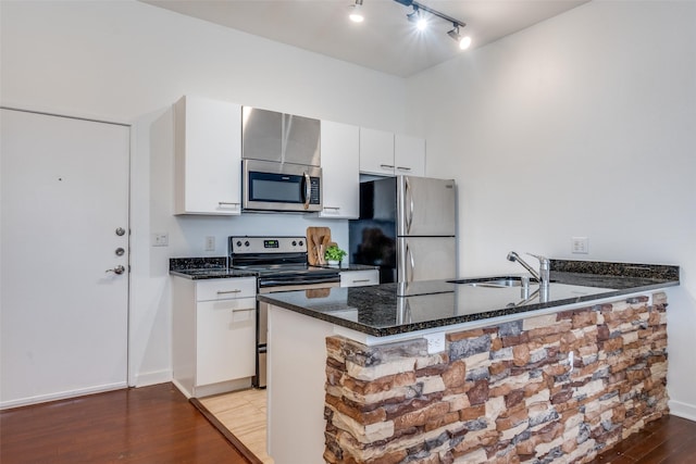 kitchen featuring white cabinets, appliances with stainless steel finishes, dark stone countertops, kitchen peninsula, and hardwood / wood-style flooring