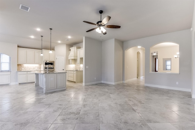 kitchen featuring decorative backsplash, hanging light fixtures, a kitchen island with sink, ceiling fan, and stainless steel microwave