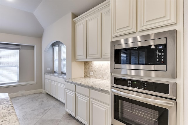 kitchen featuring light stone counters, white cabinets, appliances with stainless steel finishes, and lofted ceiling