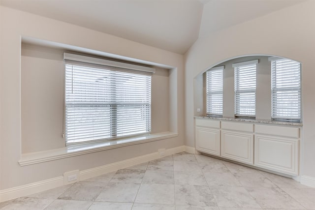 tiled empty room featuring lofted ceiling