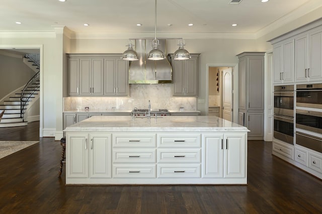 kitchen featuring hanging light fixtures, light stone countertops, an island with sink, and gray cabinetry