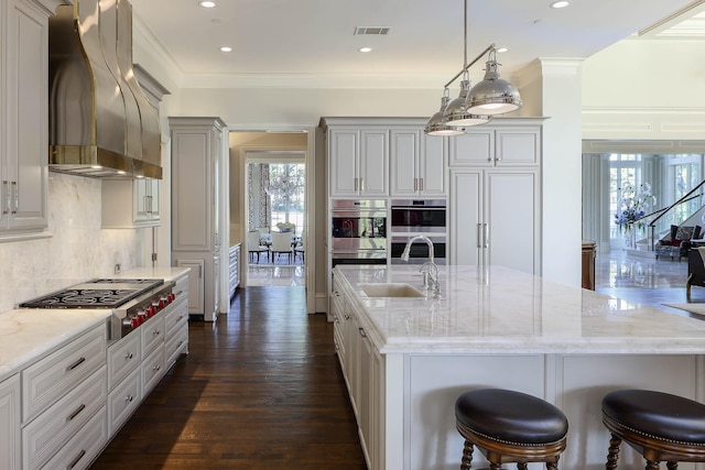 kitchen featuring a kitchen bar, a center island with sink, stainless steel appliances, hanging light fixtures, and custom range hood