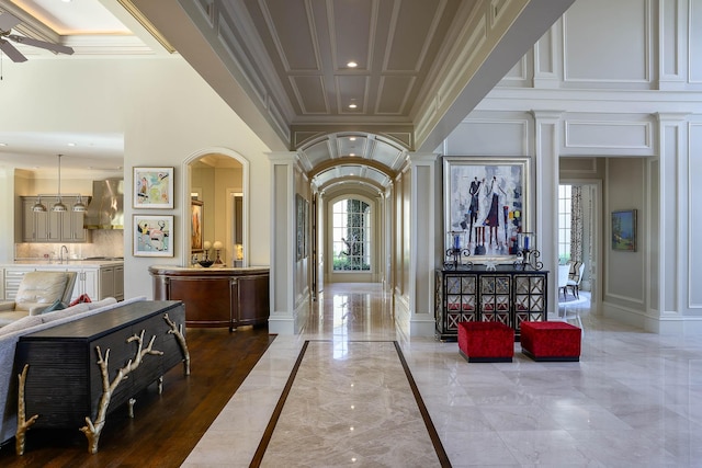 foyer featuring ceiling fan, sink, ornamental molding, and ornate columns