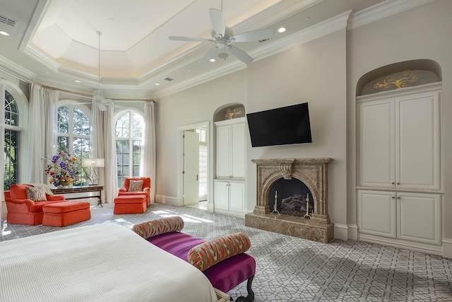 carpeted bedroom with ceiling fan, a fireplace, a tray ceiling, and ornamental molding