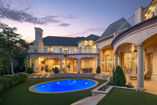 pool at dusk featuring ceiling fan, a patio area, and a yard