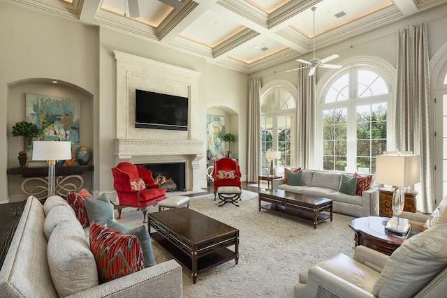 living room featuring ceiling fan, beamed ceiling, a high ceiling, crown molding, and coffered ceiling