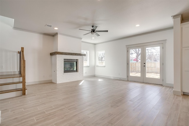 unfurnished living room with ceiling fan, a brick fireplace, light hardwood / wood-style flooring, ornamental molding, and french doors