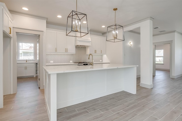 kitchen with decorative light fixtures, white cabinets, a kitchen island with sink, and backsplash