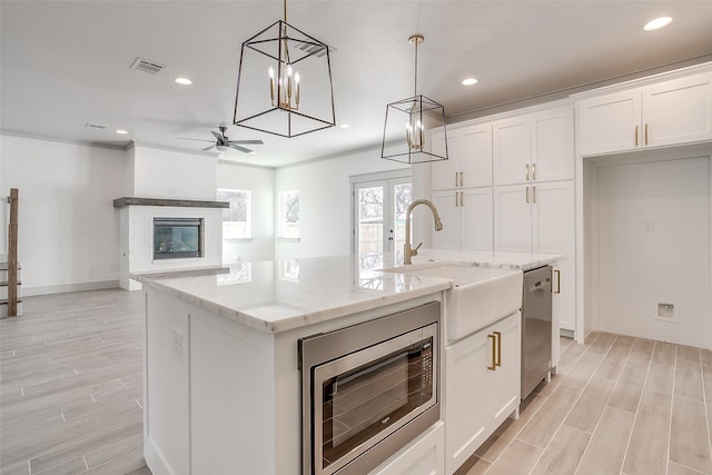 kitchen with pendant lighting, white cabinets, stainless steel appliances, an island with sink, and light stone counters