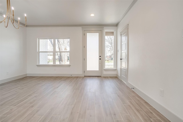 empty room with a wealth of natural light, crown molding, a chandelier, and light hardwood / wood-style floors