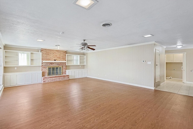 unfurnished living room featuring a brick fireplace, a textured ceiling, built in features, and light hardwood / wood-style flooring