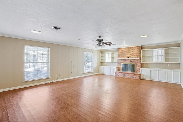 unfurnished living room featuring ceiling fan, a fireplace, hardwood / wood-style floors, a textured ceiling, and built in shelves