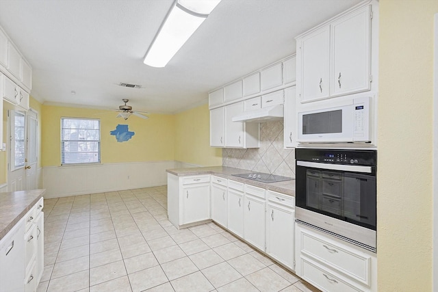 kitchen with white cabinets, white microwave, tasteful backsplash, kitchen peninsula, and oven