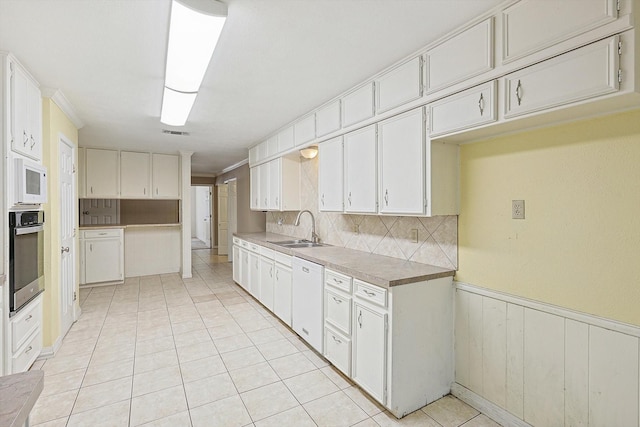 kitchen with backsplash, oven, sink, white dishwasher, and white cabinetry