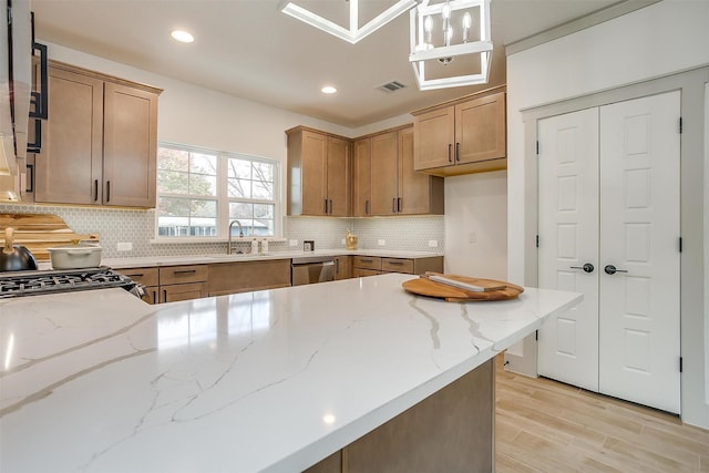 kitchen with light hardwood / wood-style floors, dishwasher, hanging light fixtures, light stone counters, and sink