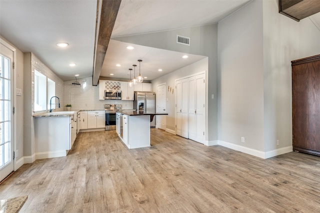 kitchen with appliances with stainless steel finishes, pendant lighting, white cabinetry, a center island, and light hardwood / wood-style flooring