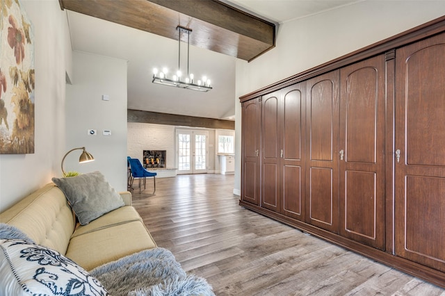 living room with french doors, beam ceiling, a chandelier, a fireplace, and light hardwood / wood-style floors