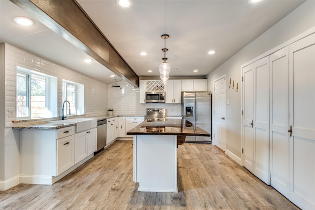 kitchen featuring pendant lighting, sink, stainless steel appliances, white cabinets, and a kitchen island