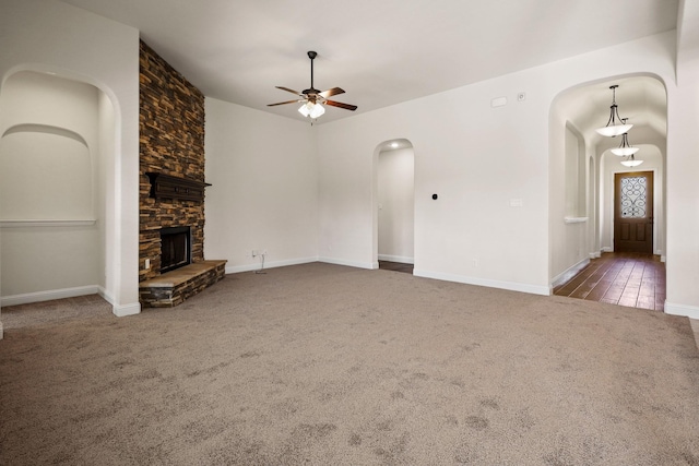 unfurnished living room featuring ceiling fan, dark carpet, and a stone fireplace