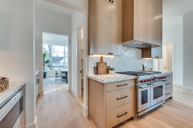 kitchen with light brown cabinetry, double oven range, backsplash, and light hardwood / wood-style floors