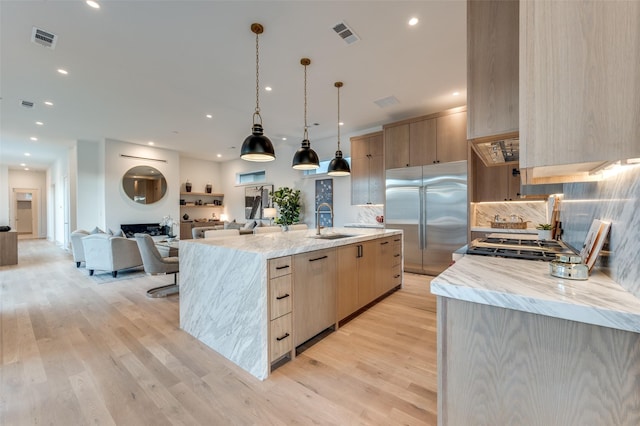 kitchen featuring decorative light fixtures, sink, stainless steel built in fridge, light brown cabinets, and a large island