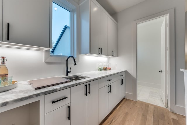 kitchen featuring white cabinetry, light hardwood / wood-style floors, light stone counters, and sink