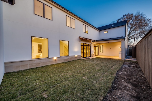 back house at dusk with ceiling fan, a patio area, and a lawn