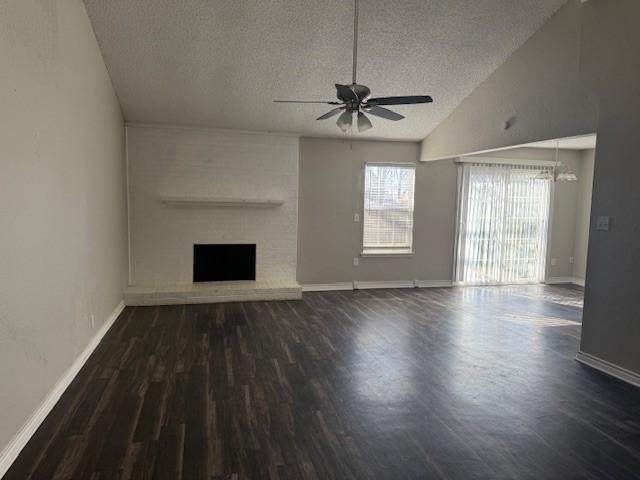 unfurnished living room featuring ceiling fan with notable chandelier, dark hardwood / wood-style flooring, beamed ceiling, high vaulted ceiling, and a brick fireplace