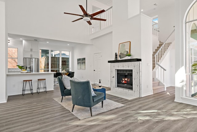 living room with ceiling fan, a high ceiling, light wood-type flooring, and a fireplace